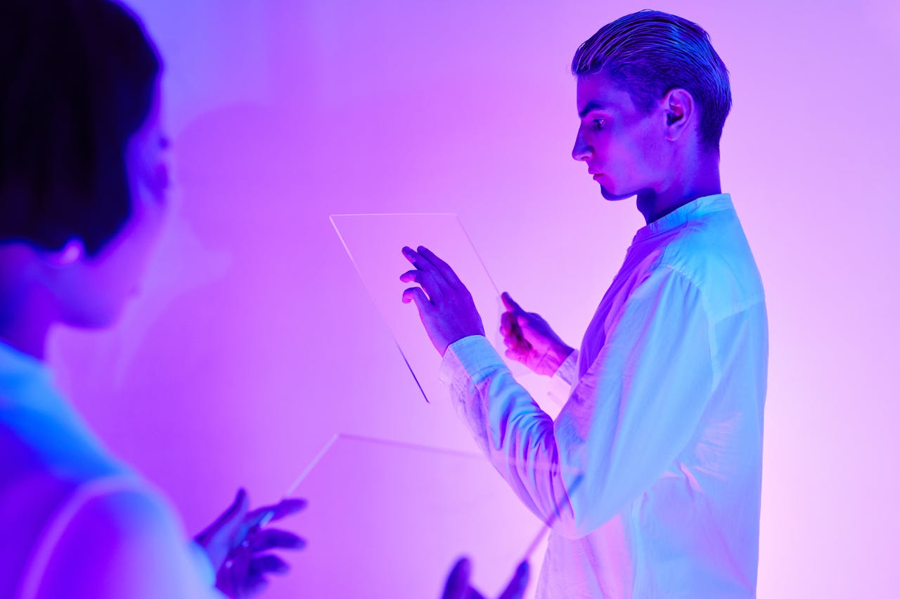 Two individuals engaging with futuristic transparent touch screens in a vibrant purple-lit studio.